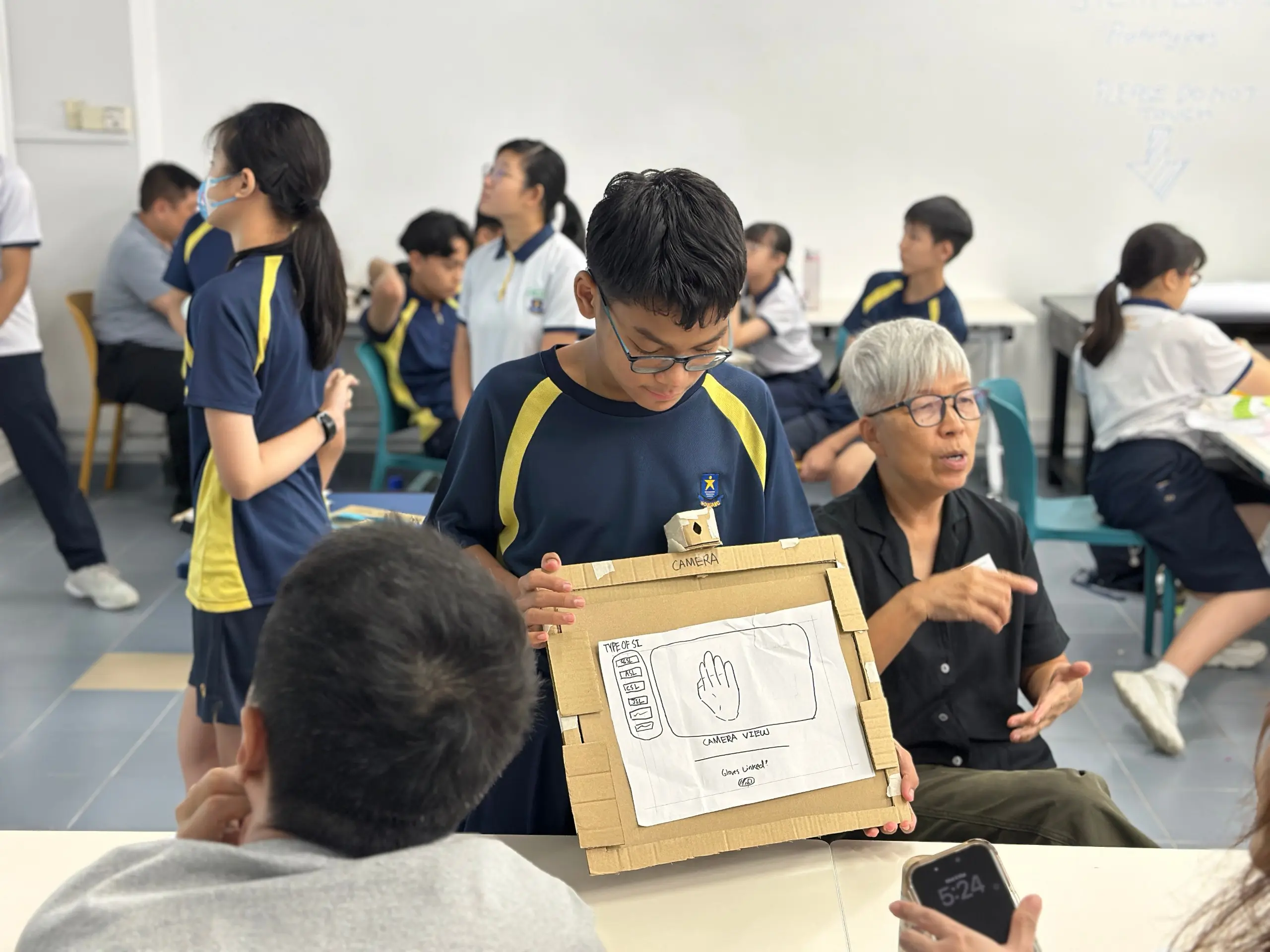 A student with the help of an interpreter presenting a design prototype for the deaf community to a member of the SADeaf community