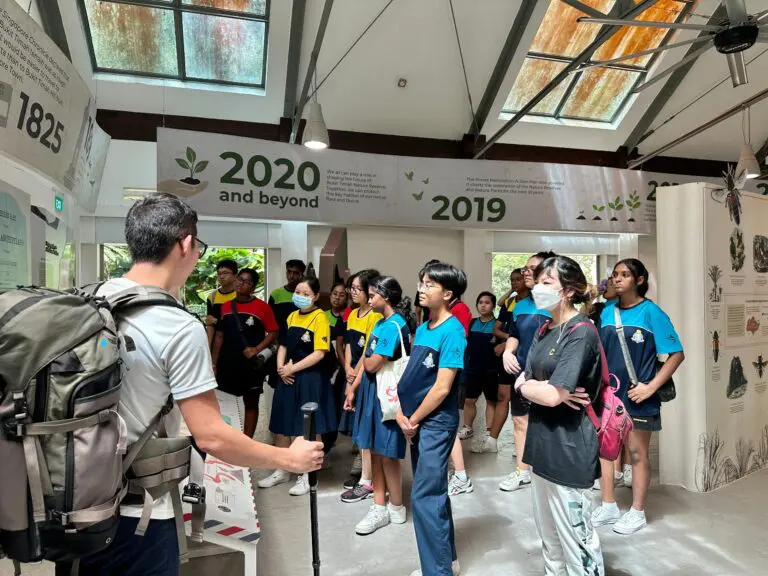 community-design-thinking-workshop-cover - C-Academy Group of students in colorful uniforms listening to a guide inside a nature exhibit, with a '2020 and beyond' banner overhead.