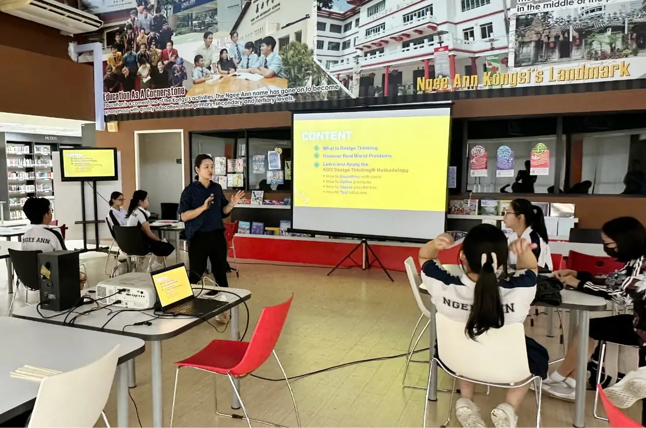 Instructor presents a yellow 'CONTENT' slide to a classroom of students seated at tables in a library setting.